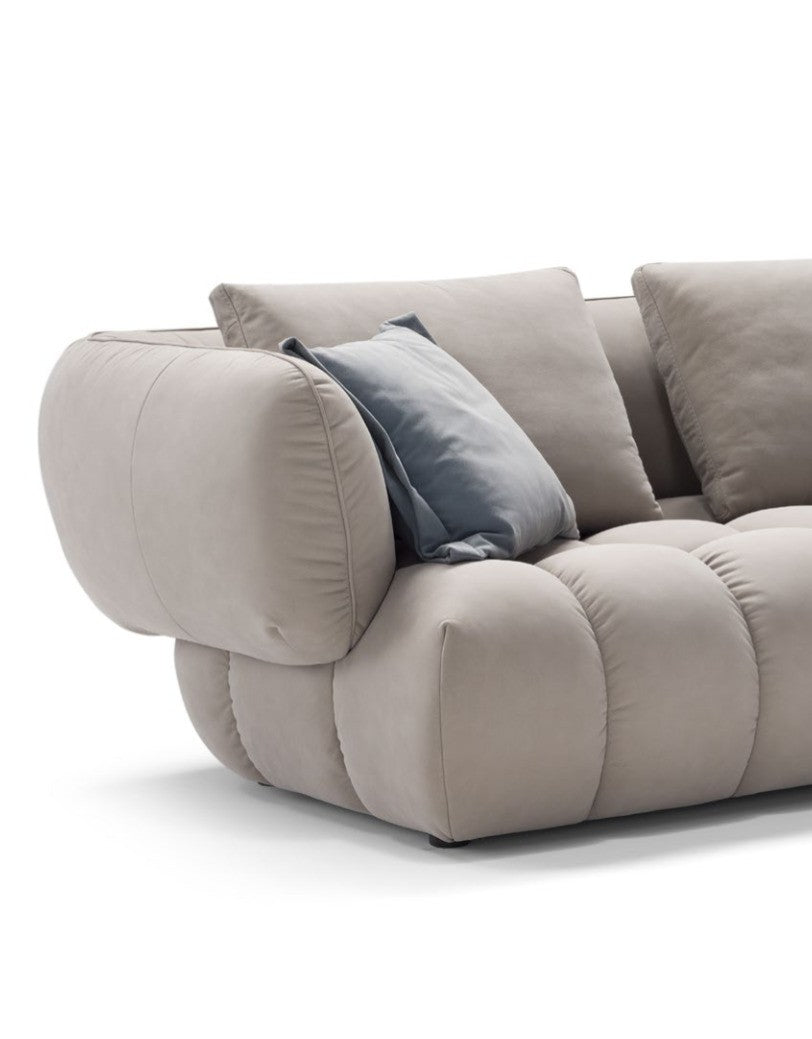 Close-up of the Abbracci sofa's padded armrest, quilted seat cushions and blue accent pillow