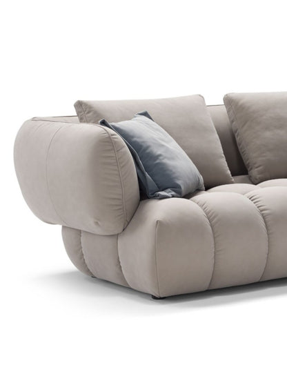 Close-up of the Abbracci sofa's padded armrest, quilted seat cushions and blue accent pillow