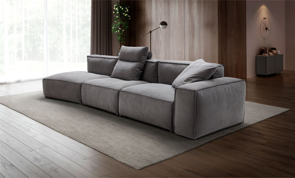 Grey modular sectional sofa with loose back cushions in a warm, wood-paneled living room