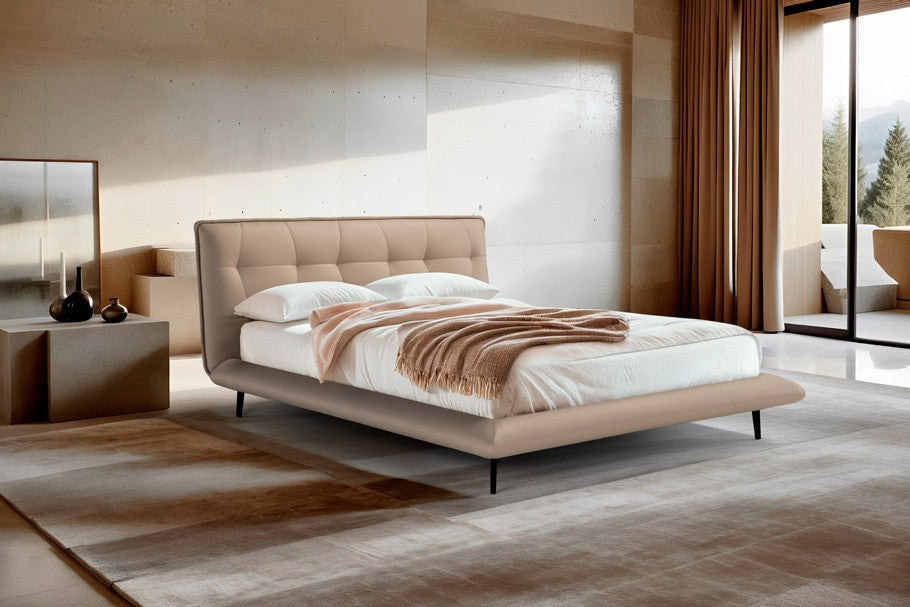 Borg Bed with tufted curved headboard in beige leather, styled in a warm minimalist bedroom with a stone-wall backdrop