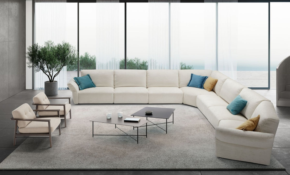 Ivory fabric corner sectional sofa with ottoman in a bright living room with floor-to-ceiling windows