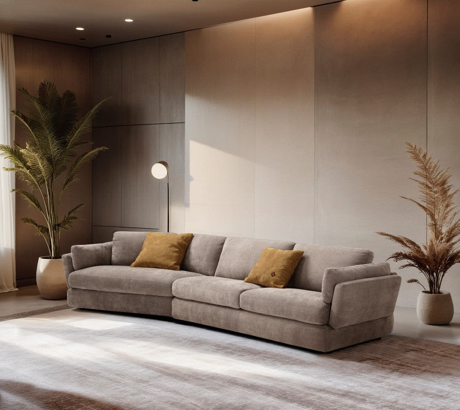 Dambo sofa in taupe fabric with an angled element, styled in a warm living room with ochre cushions