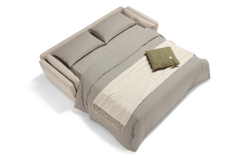 Dambo sofa bed in beige fabric opened into a bed with pillows, sheets and a throw