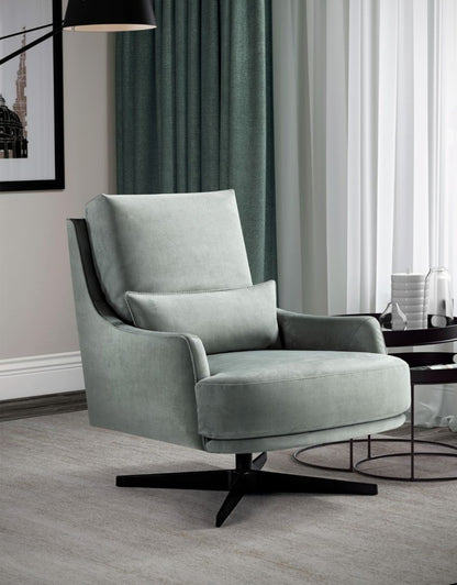 Filicudi armchair in pale sage fabric on a black swivel base, three-quarter view in a living room with teal curtains