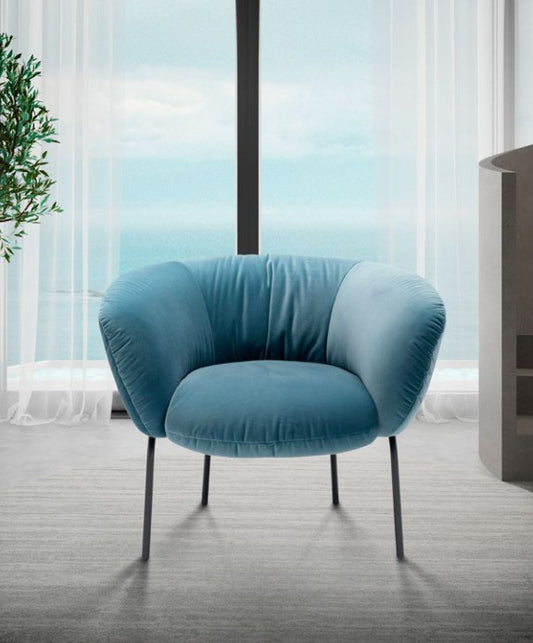 Front view of the Jill armchair in blue velvet beside a floor-to-ceiling window
