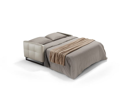 Mal sofa bed fully opened into a bed with mattress, pillows and throw, leather tufted armrest and metal base visible