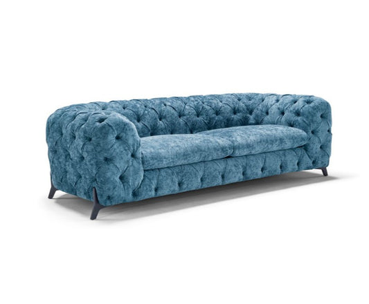 Blue fabric tufted Chesterfield sofa, angled front view showing seat cushions, on white background