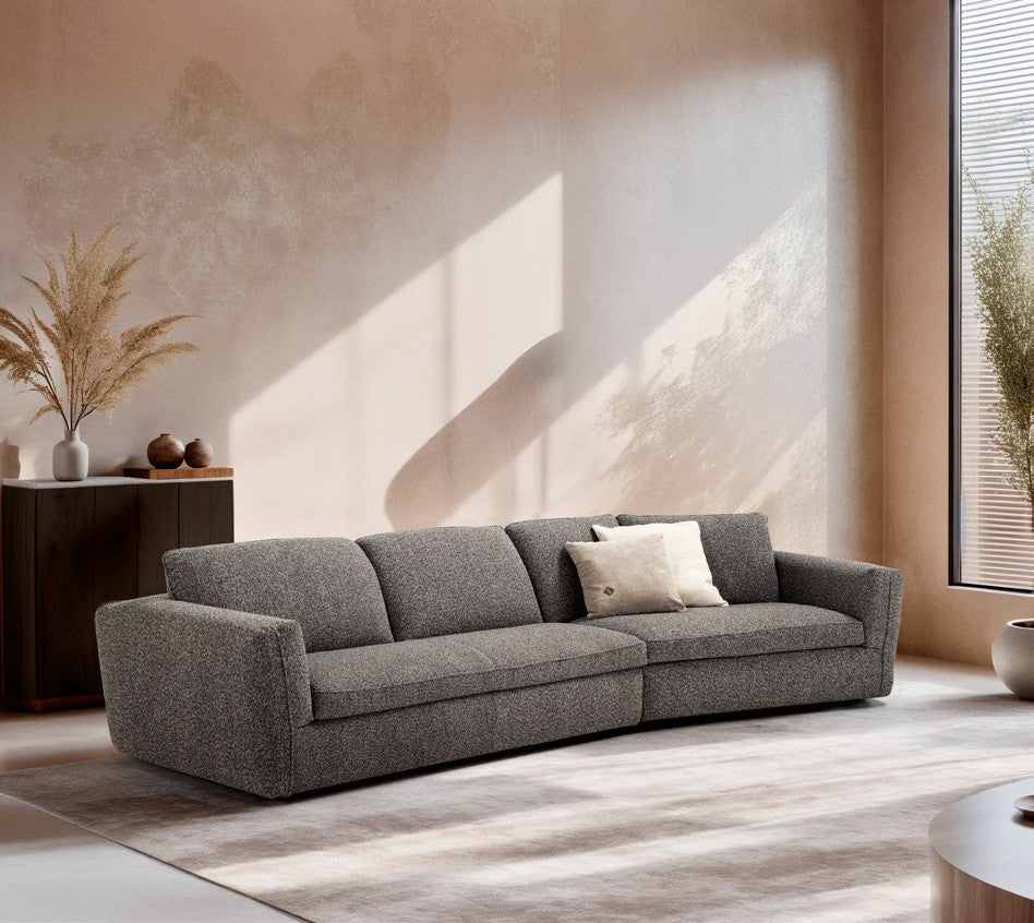 Siria sofa bed in grey boucle fabric with a curved angled element, in a sunlit living room with plaster walls