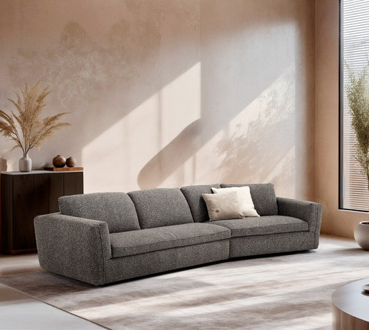 Siria sofa bed in grey boucle fabric with a curved angled element, in a sunlit living room with plaster walls