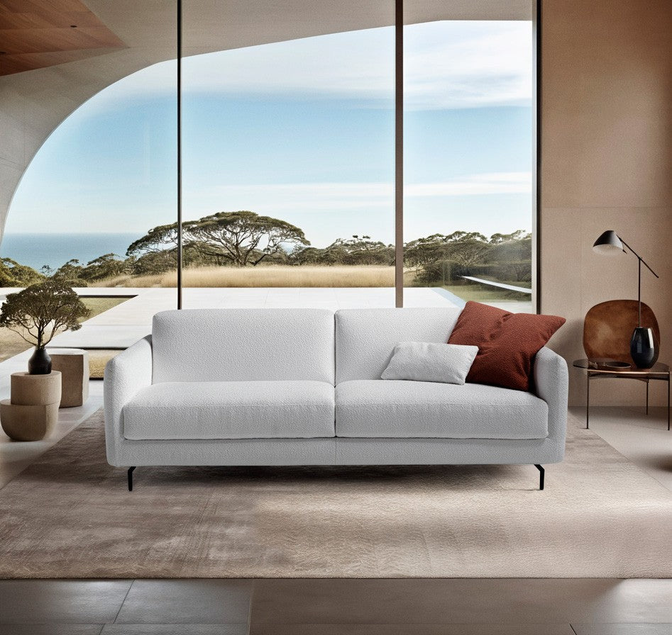 Solar sofa bed in white boucle fabric with slender black metal legs in a bright living room overlooking the sea