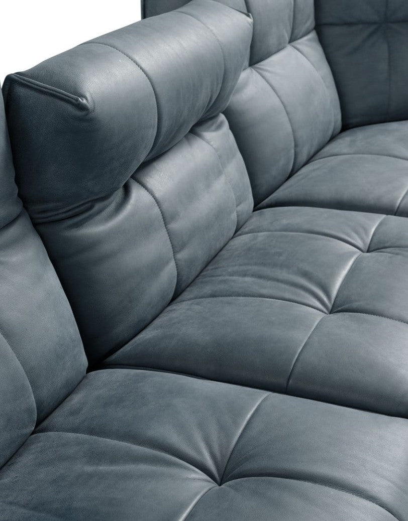 Close-up of the square quilting on the seat, backrest and armrest of the Sospiro sofa in blue-grey leather