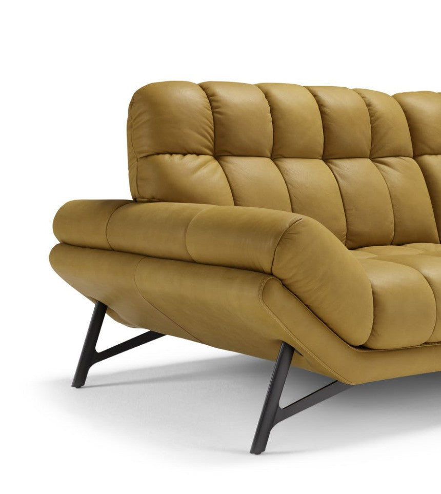Close-up of the Spiga sofa in mustard leather showing the soft quilting, inclined armrest and slanted metal leg